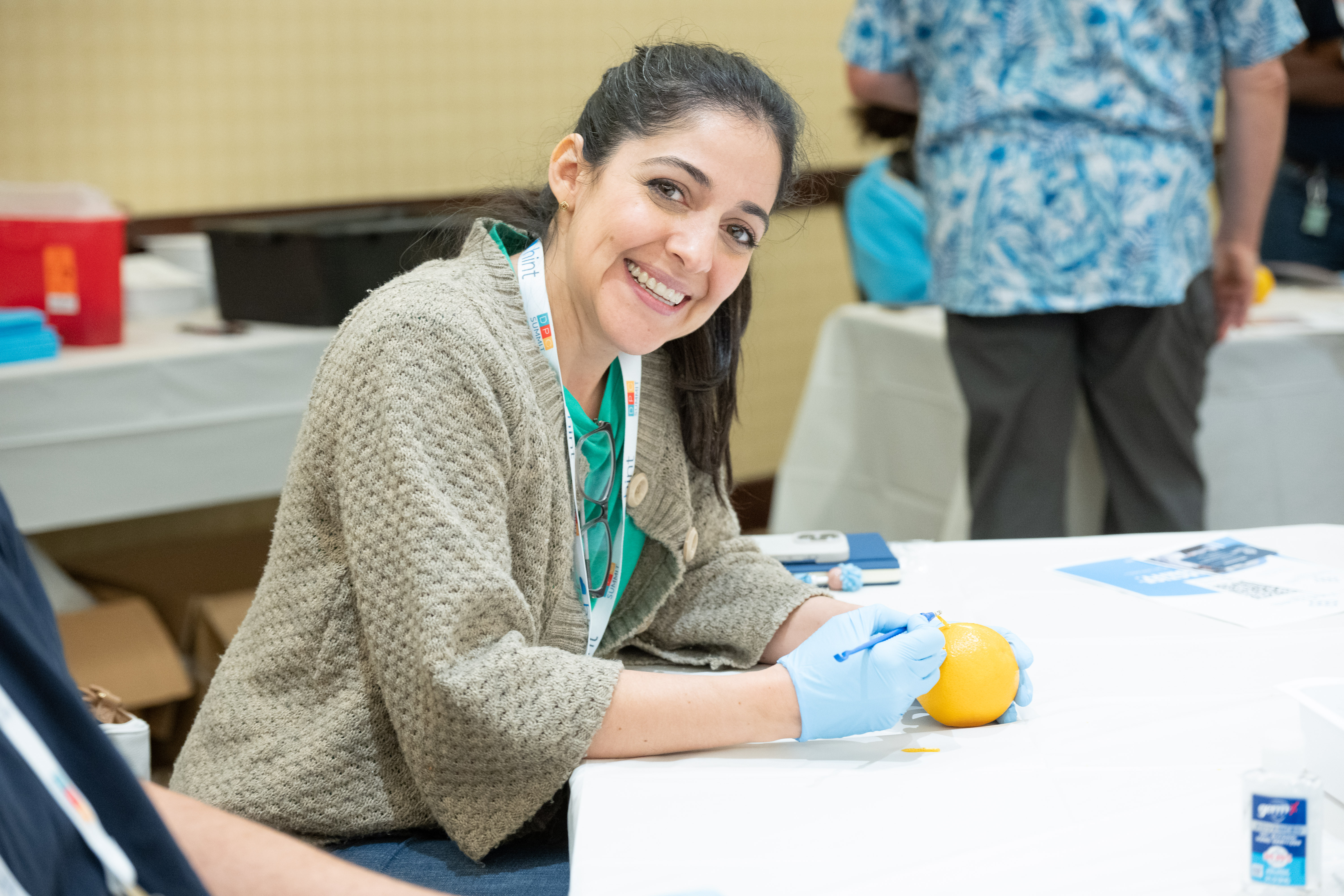 Doctor practicing sutures on orange while smiling at camera